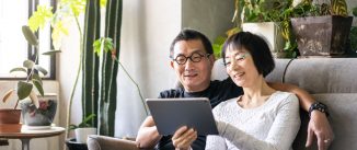 A man and woman look at a tablet while sitting on a couch in their home